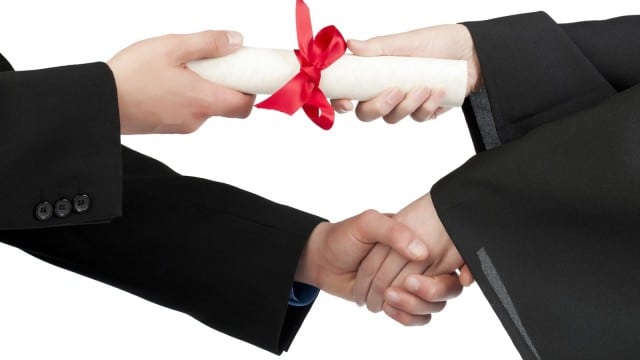 Close up image of graduating student hand accepting diploma against against white background