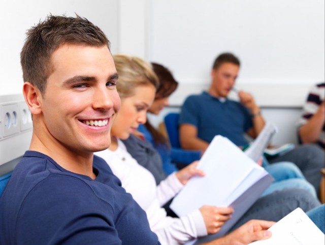 Happy young man sitting in class reading