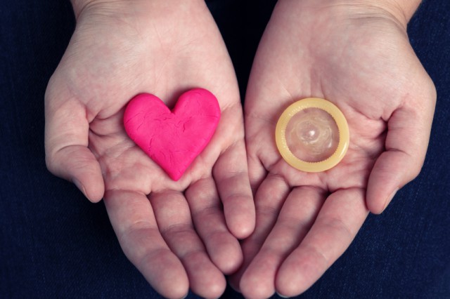 Woman's hands hold a heart shape and a condom. Concept image.