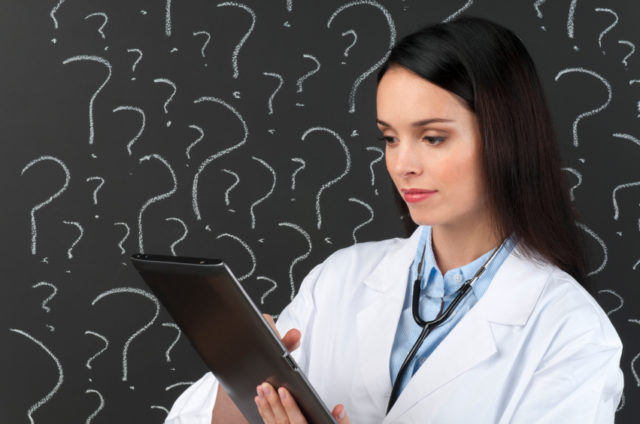 Female doctor with digital tablet in front of question marks on blackboard