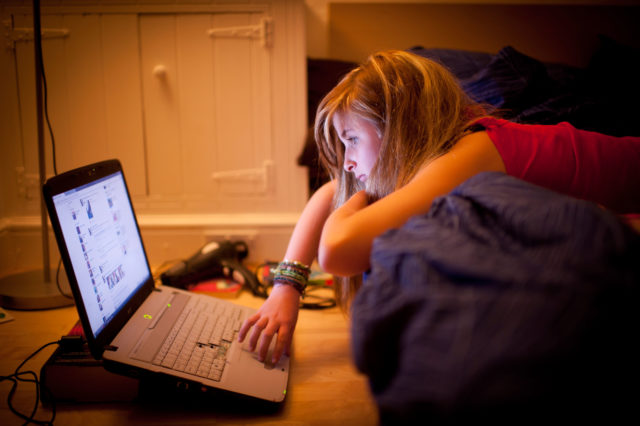 C6YB19 a 12 twelve 13 thirteen year old teenage girl on bed in her bedroom at night reading Facebook page on laptop computer UK