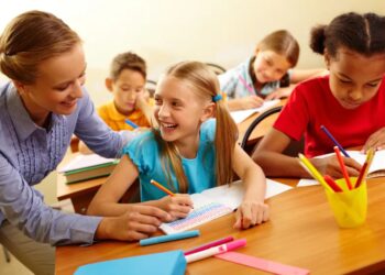 Portrait of smart girl and her teacher looking at each other at lesson in classroom