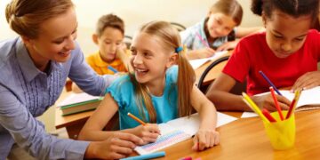 Portrait of smart girl and her teacher looking at each other at lesson in classroom