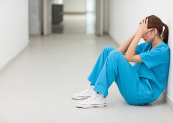 Nurse sitting in a corridor while holding her head