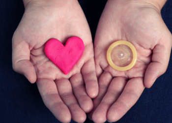 Woman's hands hold a heart shape and a condom. Concept image.