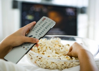 Person watching television, holding remote control and bowl of popcorn, cropped view --- Image by © Ale Ventura/PhotoAlto/Corbis