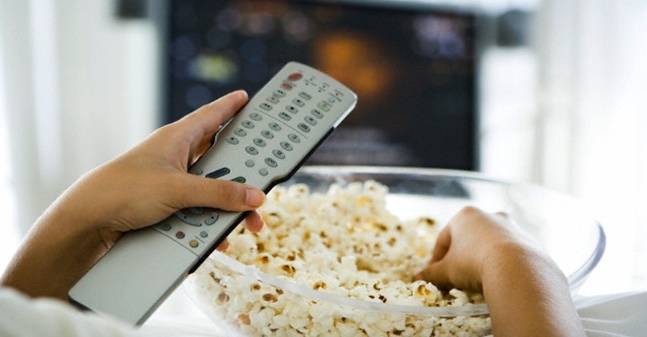 person watching television holding remote control and bowl of popcorn cropped view