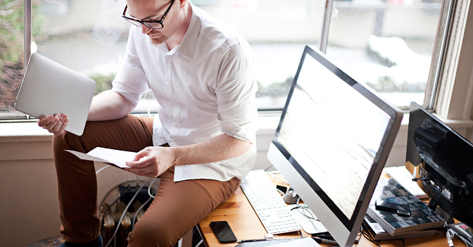 freelancer sitting on desk reviewing paperwork and holding tablet