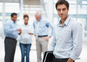 Handsome young business man with a laptop and colleagues at the background