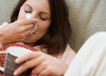 Woman with tissue and hot drink --- Image by © Royalty-Free/Corbis