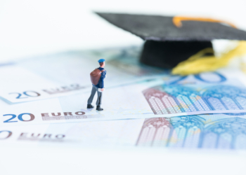 Miniature man standing on top of 20 Euro banknotes and mortar board close up