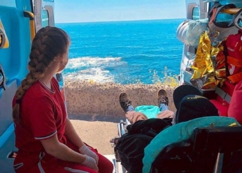 Una volontaria della Croce Rossa e un uomo in barella guardano il mare da un'ambulanza