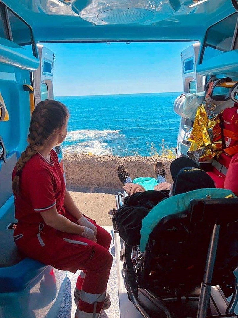 Una volontaria della Croce Rossa e un uomo in barella guardano il mare da un'ambulanza