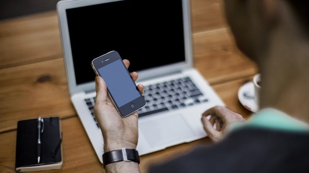 Un ragazzo al computer guarda il suo smartphone