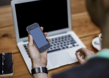 Un ragazzo al computer guarda il suo smartphone