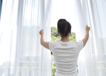 Asian young woman opening the curtains to a new day.