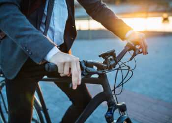 Midsection of businessman commuter with electric bicycle traveling home from work in city.