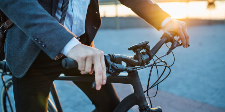 midsection of businessman commuter with electric bicycle traveling from work in city