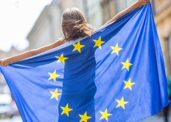 EU Flag. Cute happy girl with the flag of the European Union. Young teenage girl waving with the European Union flag in the city.