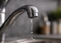 Close-up of a dripping chrome kitchen faucet with falling water drop in a sink, illustrating water waste and conservation issues